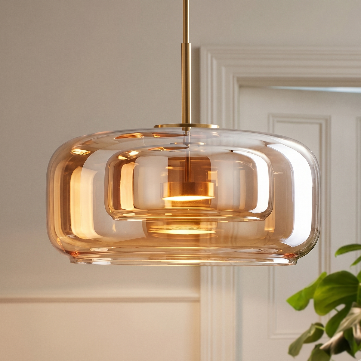 Gros plan sur une suspension en verre ambré à double cloche, avec tige et douille en laiton doré, diffusant une lumière chaude et cuivrée.